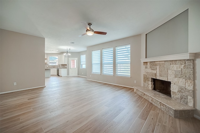 unfurnished living room featuring light hardwood / wood-style flooring, a stone fireplace, and ceiling fan with notable chandelier