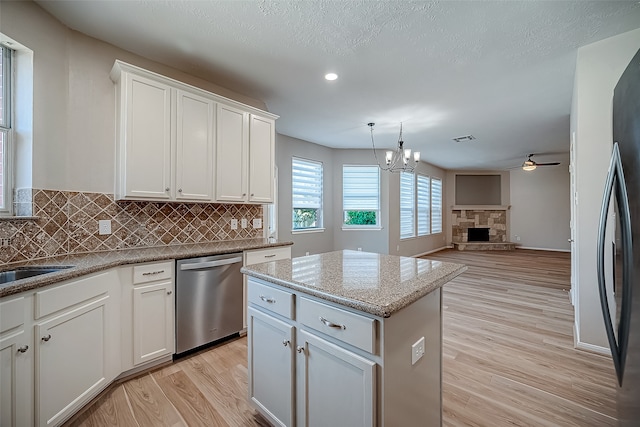 kitchen featuring dishwasher, a stone fireplace, light wood-type flooring, white cabinets, and ceiling fan with notable chandelier