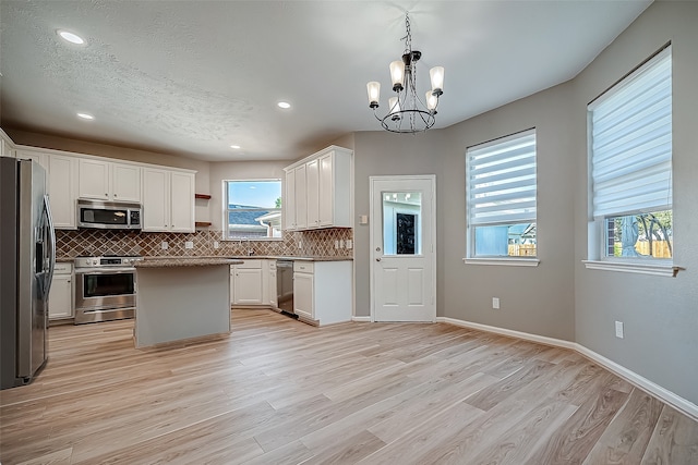 kitchen with appliances with stainless steel finishes, a center island, hanging light fixtures, white cabinetry, and light hardwood / wood-style flooring