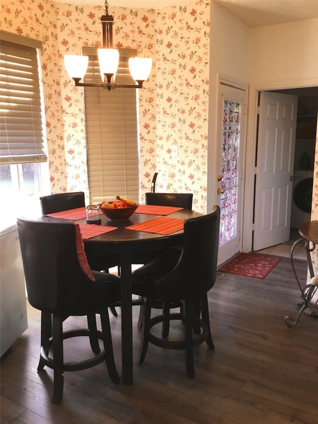 dining space featuring wood finished floors, wallpapered walls, washer / dryer, and a chandelier