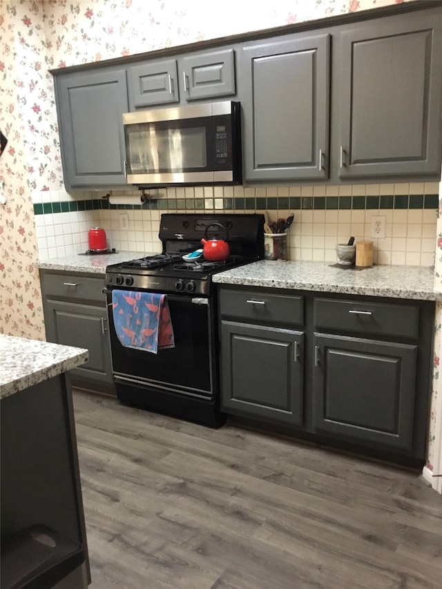 kitchen featuring black gas stove, gray cabinetry, light stone countertops, dark hardwood / wood-style flooring, and tasteful backsplash