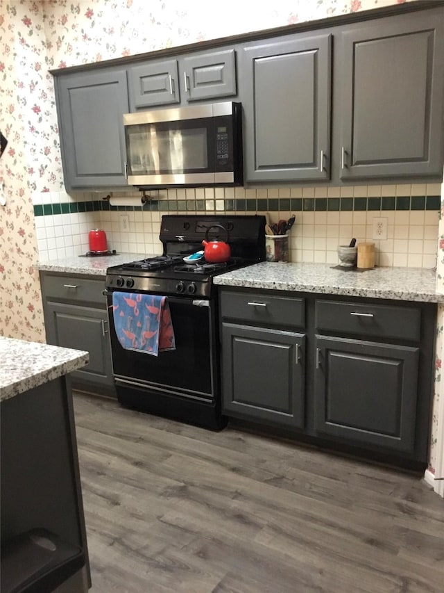 kitchen featuring stainless steel microwave, black range with gas stovetop, wallpapered walls, tasteful backsplash, and gray cabinetry