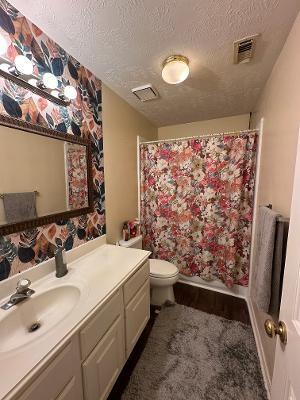 full bathroom featuring a textured ceiling, toilet, vanity, wallpapered walls, and baseboards