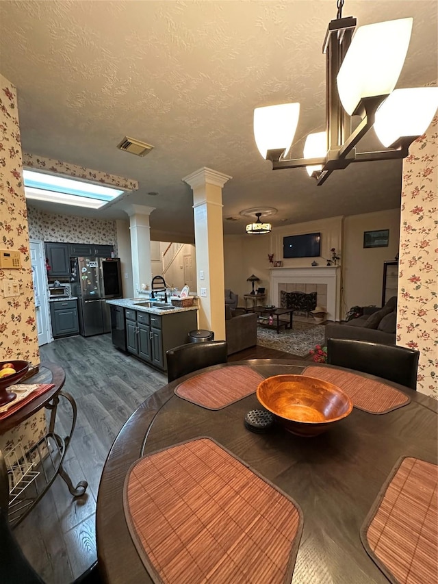 dining room with decorative columns, dark wood finished floors, wallpapered walls, a fireplace, and a textured ceiling
