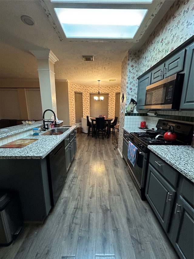 kitchen with appliances with stainless steel finishes, sink, backsplash, pendant lighting, and hardwood / wood-style flooring