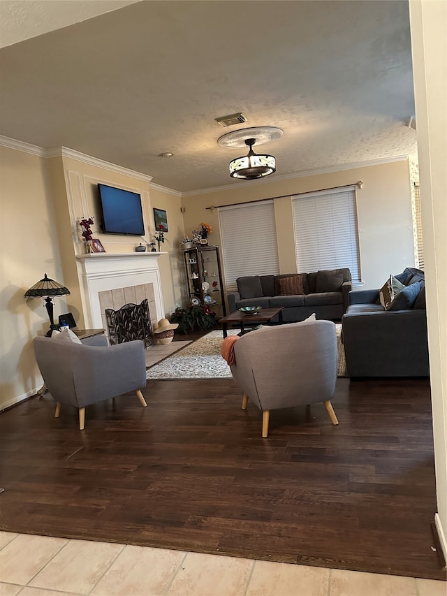 living room with ornamental molding, a textured ceiling, hardwood / wood-style flooring, and a tile fireplace