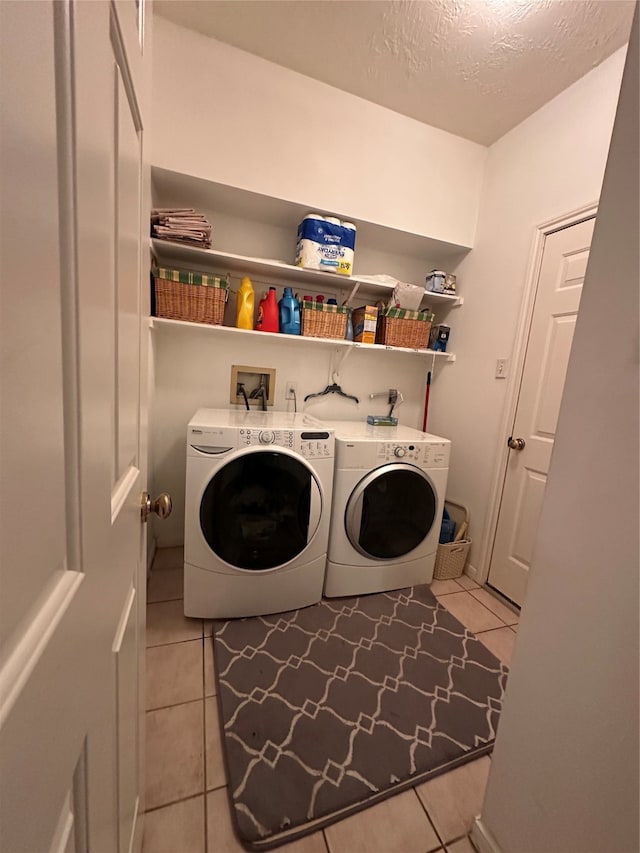 clothes washing area featuring a textured ceiling, washer and clothes dryer, and light tile patterned floors