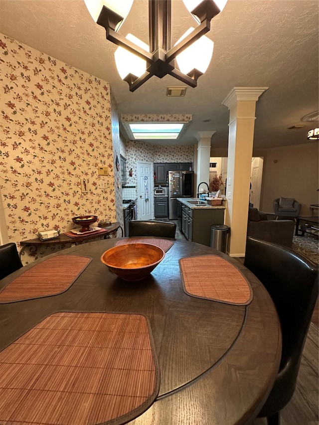 dining space featuring sink, a textured ceiling, a chandelier, and decorative columns