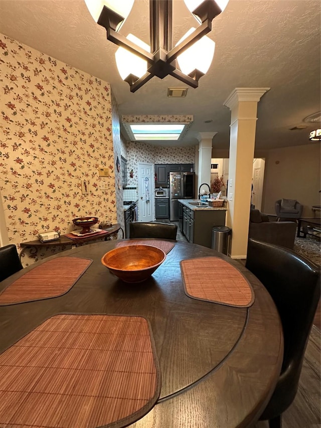 dining area featuring wallpapered walls, decorative columns, a textured ceiling, dark wood-style floors, and a chandelier
