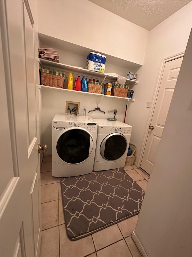 clothes washing area with separate washer and dryer, light tile patterned floors, and a textured ceiling