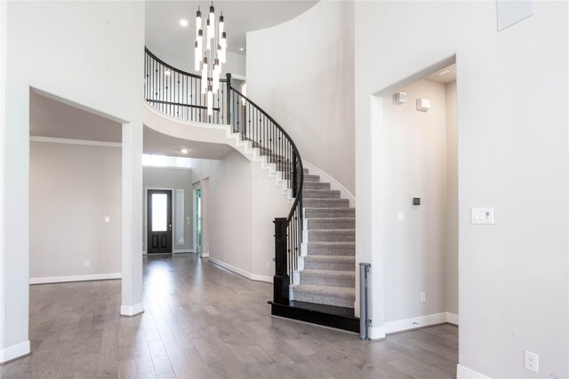 entrance foyer with a towering ceiling, a notable chandelier, hardwood / wood-style floors, and ornamental molding