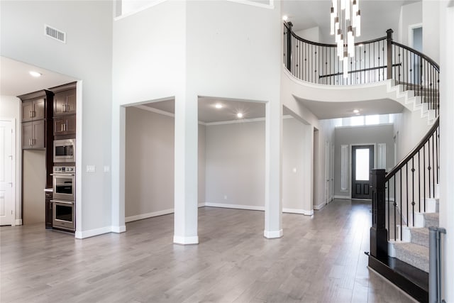 foyer entrance with an inviting chandelier, a high ceiling, crown molding, and light hardwood / wood-style floors