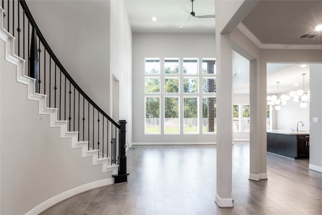 entrance foyer with an inviting chandelier, ornamental molding, wood-type flooring, and a healthy amount of sunlight