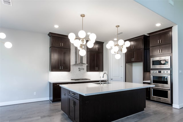 kitchen featuring an island with sink, sink, pendant lighting, appliances with stainless steel finishes, and light hardwood / wood-style floors