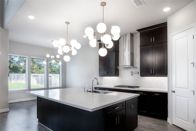 kitchen featuring a kitchen island with sink, wall chimney exhaust hood, backsplash, sink, and light hardwood / wood-style floors