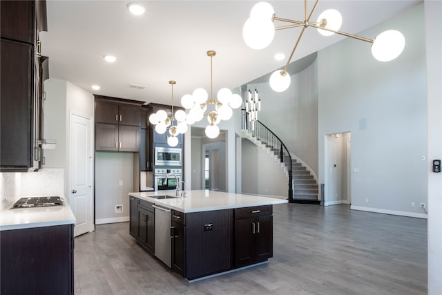 kitchen featuring appliances with stainless steel finishes, dark brown cabinetry, pendant lighting, hardwood / wood-style flooring, and a center island with sink