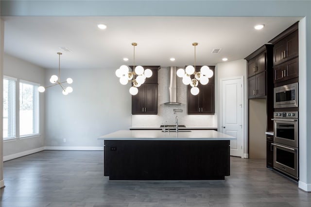 kitchen with wall chimney exhaust hood, decorative backsplash, a center island with sink, and pendant lighting