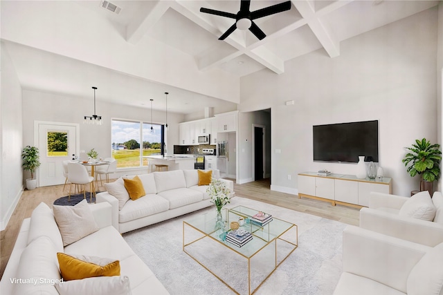 living room featuring ceiling fan with notable chandelier, beamed ceiling, a towering ceiling, and light hardwood / wood-style flooring