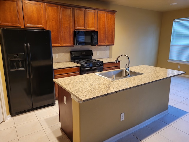 kitchen with an island with sink, black appliances, sink, and light tile patterned floors