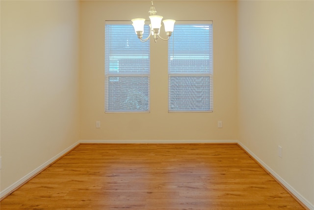 spare room with a notable chandelier and light wood-type flooring