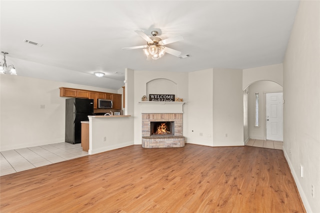 unfurnished living room featuring a brick fireplace, ceiling fan with notable chandelier, and light hardwood / wood-style floors