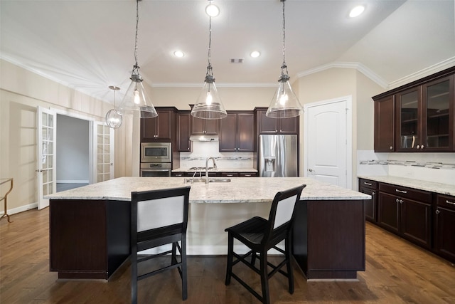 kitchen featuring a kitchen bar, sink, decorative light fixtures, a center island with sink, and stainless steel appliances