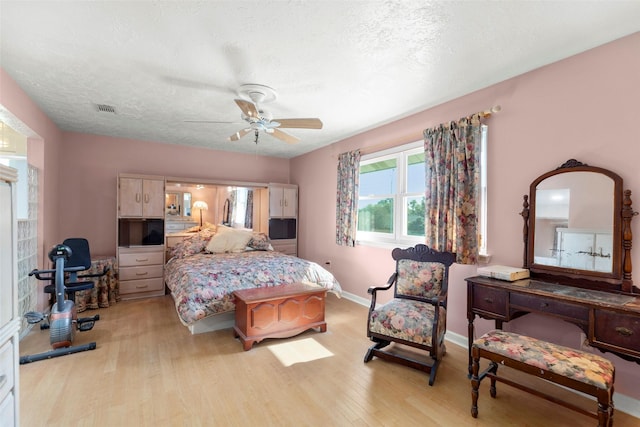 bedroom with ceiling fan, a textured ceiling, and light wood-type flooring