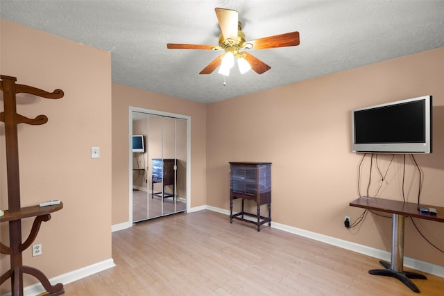 miscellaneous room featuring ceiling fan, light hardwood / wood-style flooring, and a textured ceiling