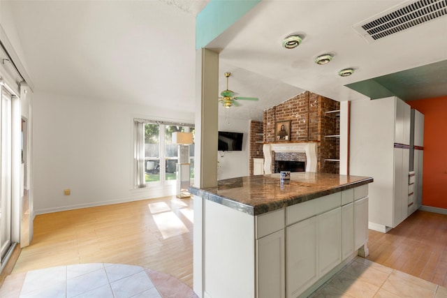 kitchen with a fireplace, lofted ceiling, dark stone countertops, white cabinets, and ceiling fan