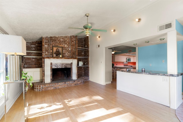 unfurnished living room featuring vaulted ceiling, a textured ceiling, light wood-type flooring, ceiling fan, and a fireplace