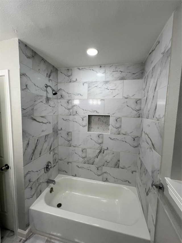 bathroom with a textured ceiling and tiled shower / bath combo