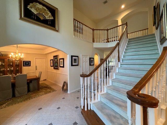 stairway with tile patterned floors, a towering ceiling, and an inviting chandelier