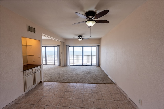 unfurnished living room with ceiling fan, light carpet, and a water view