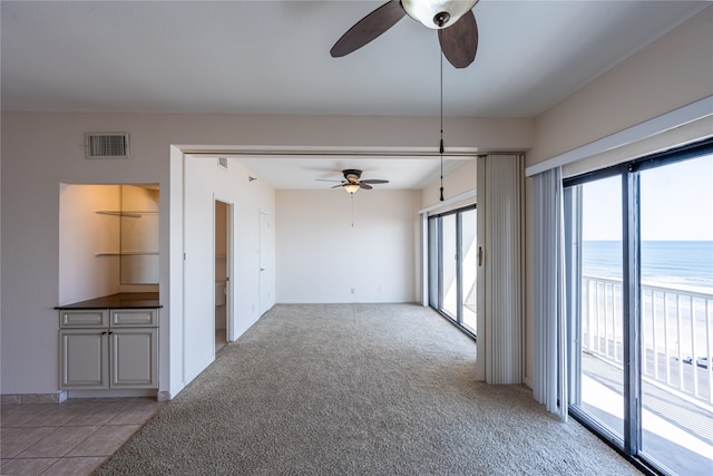 unfurnished room featuring ceiling fan, light carpet, and a water view