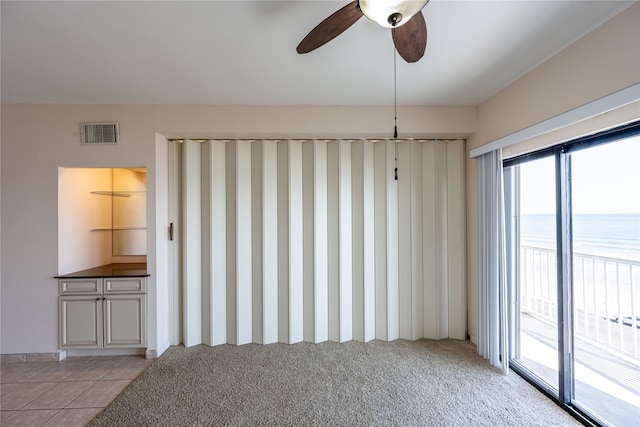 empty room featuring a water view, ceiling fan, and light tile patterned floors