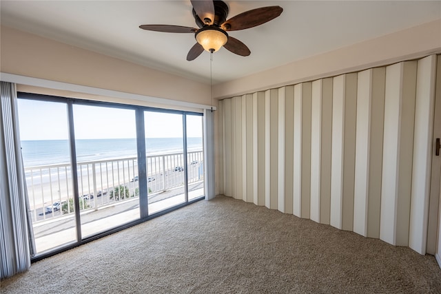 carpeted spare room with a view of the beach, a water view, and ceiling fan