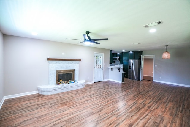 unfurnished living room with a brick fireplace, dark hardwood / wood-style flooring, and ceiling fan