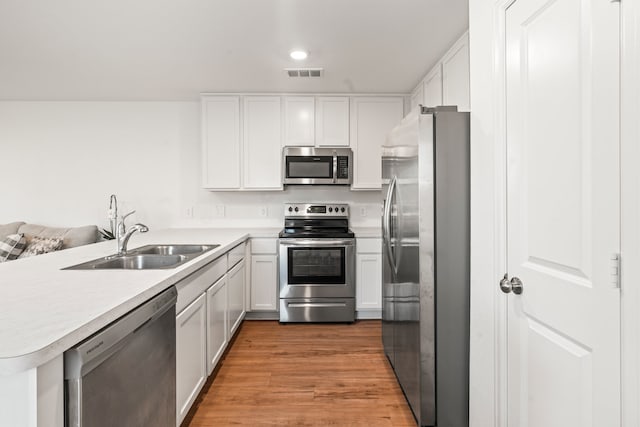 kitchen with white cabinets, appliances with stainless steel finishes, a peninsula, light countertops, and a sink