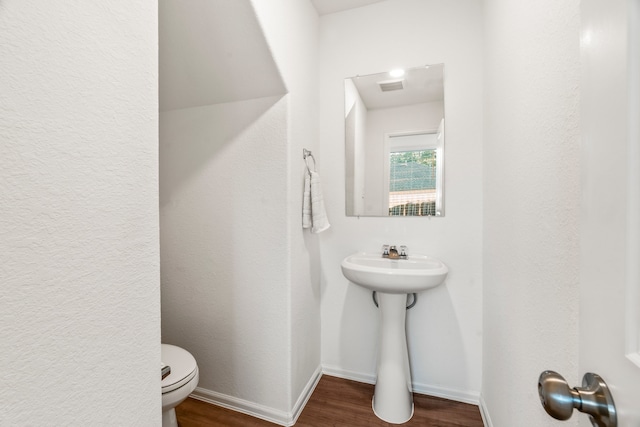 half bathroom with toilet, baseboards, visible vents, and wood finished floors