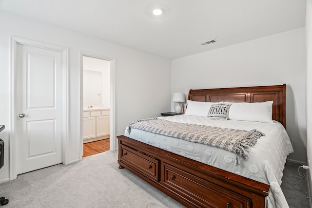 bedroom with connected bathroom, visible vents, and light colored carpet