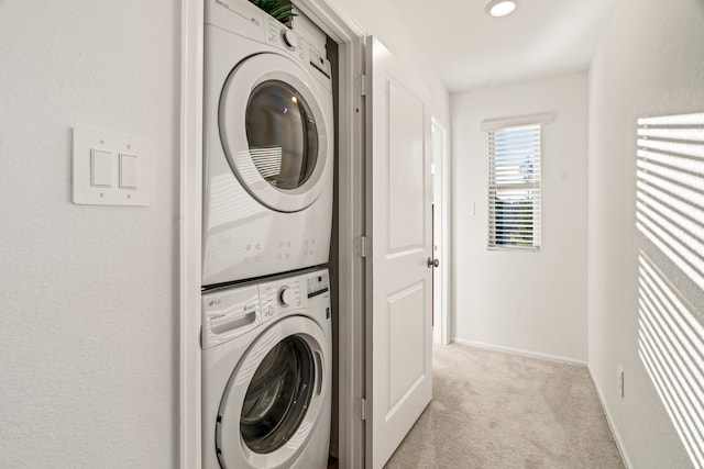 clothes washing area featuring light carpet, laundry area, stacked washer and clothes dryer, and baseboards