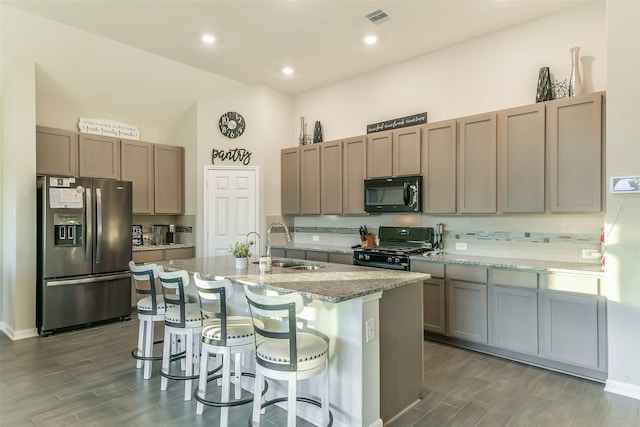 kitchen with light stone countertops, sink, dark hardwood / wood-style flooring, a center island with sink, and black appliances