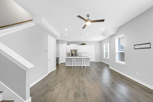 kitchen with a breakfast bar, dark hardwood / wood-style floors, white cabinets, stainless steel refrigerator with ice dispenser, and a center island with sink