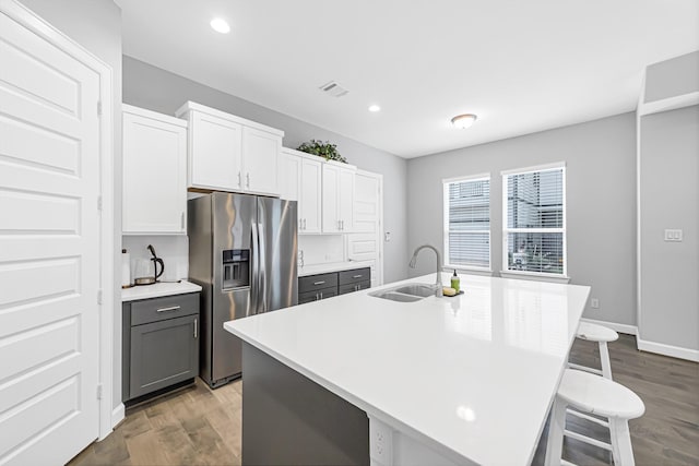 kitchen with a breakfast bar, sink, stainless steel fridge with ice dispenser, a kitchen island with sink, and white cabinets