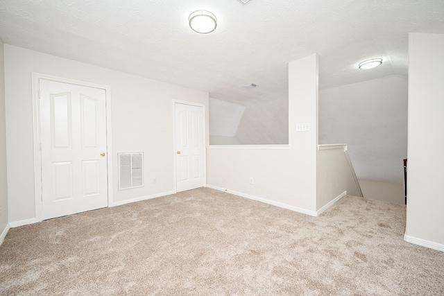 carpeted empty room featuring vaulted ceiling and a textured ceiling