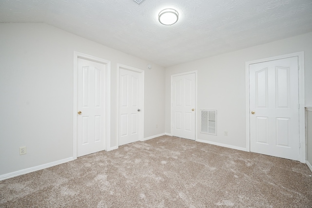 unfurnished bedroom with two closets, vaulted ceiling, carpet, and a textured ceiling