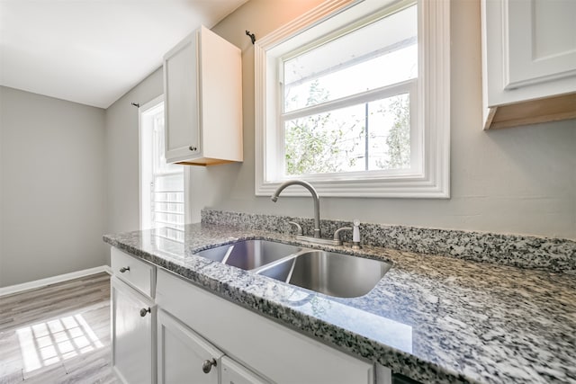 kitchen with light hardwood / wood-style flooring, white cabinets, sink, and stone countertops