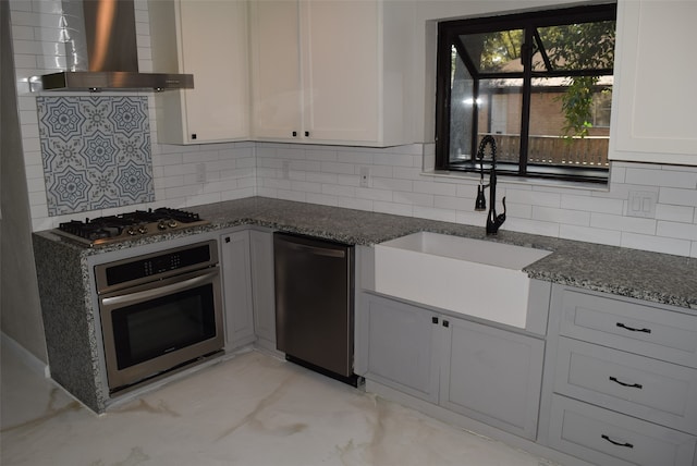 kitchen with wall chimney range hood, sink, stainless steel appliances, and white cabinets