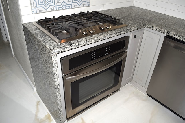 room details featuring white cabinets, stainless steel appliances, dark stone counters, and decorative backsplash