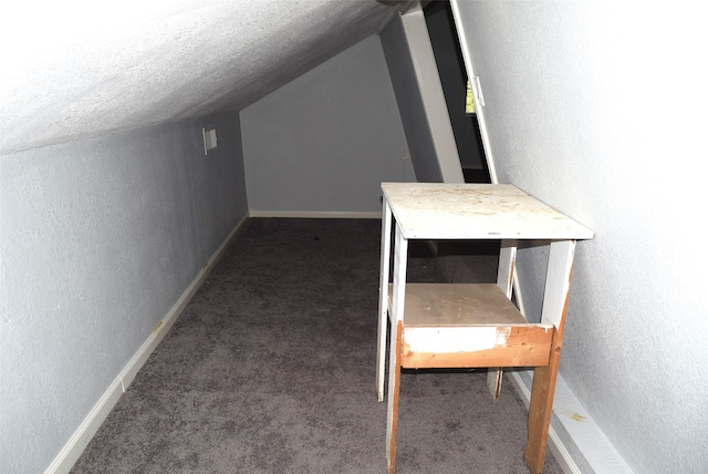 additional living space with a textured ceiling, dark colored carpet, and vaulted ceiling